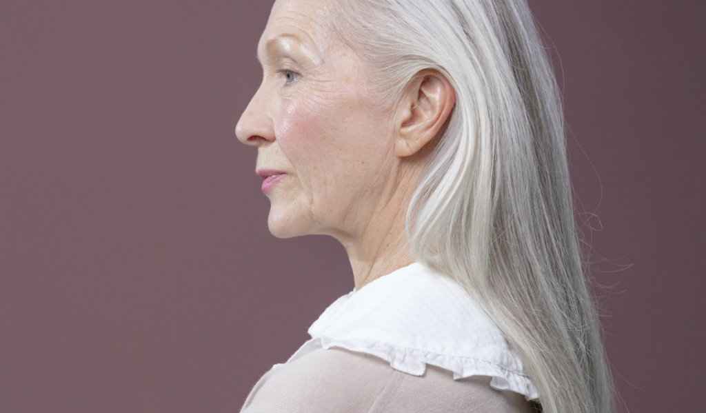 A grey-haired, middle-aged woman with wrinkles and rosy cheeks. 